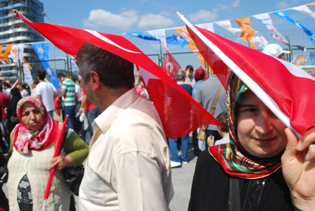 Supporters of Prime Minister Recep Tayyip Erdogan shield themselves from the midday sun with Turkish flags on their way to a rally in support of Erdoğan and the AKP. Photo: Jenna Krajeski.